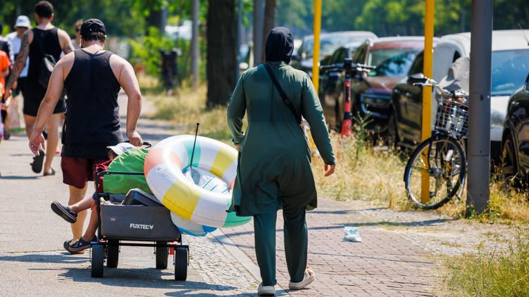  Badegäste ziehen einen Bollerwagen mit Badeutensilien nach einem Besuch im Sommerbad an Insulaner.