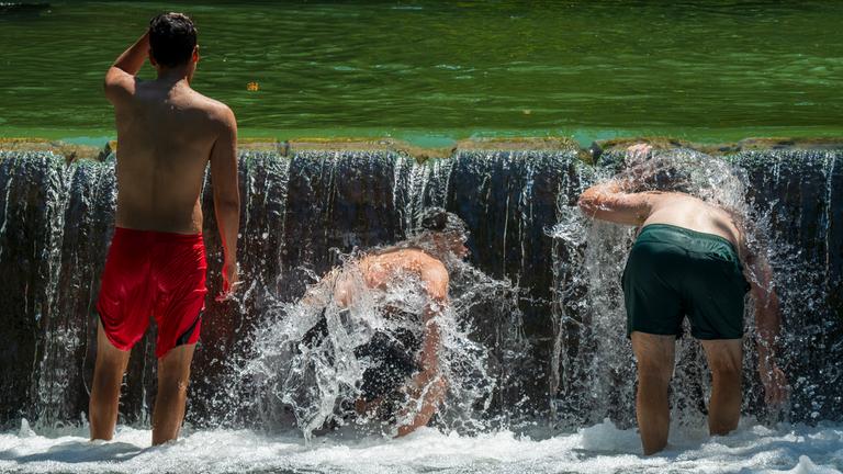 Drei Jugendliche kühlen sich im Eisbach im Englischen Garten in München ab.