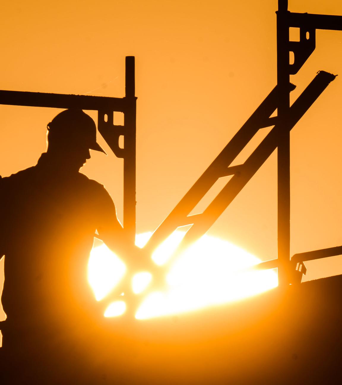 Ein Bauarbeiter steht mit einem Gasbrenner beim Bau eines Mehrfamilienhauses, als am Horizont die Sonne aufgeht