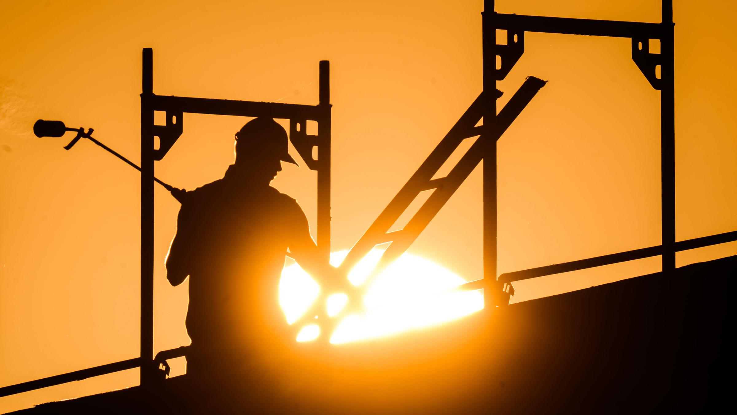 Ein Bauarbeiter steht mit einem Gasbrenner beim Bau eines Mehrfamilienhauses, als am Horizont die Sonne aufgeht