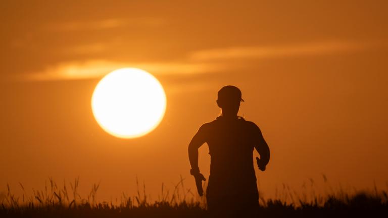 Eine Frau joggt auf einem Feldweg bei Sonnenaufgang.