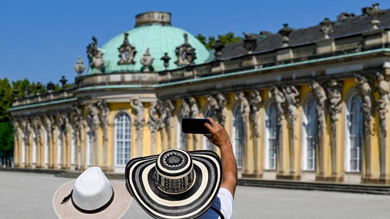  Geschützt mit ihren Sonnenhüten fotografieren Touristen aus Kolumbien vor dem Schloss Sanssouci. 