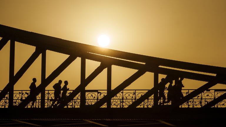 Hessen, Frankfurt am Main: Eine Gruppe joggt bei Sonnenaufgang über den Eisernen Steg. 