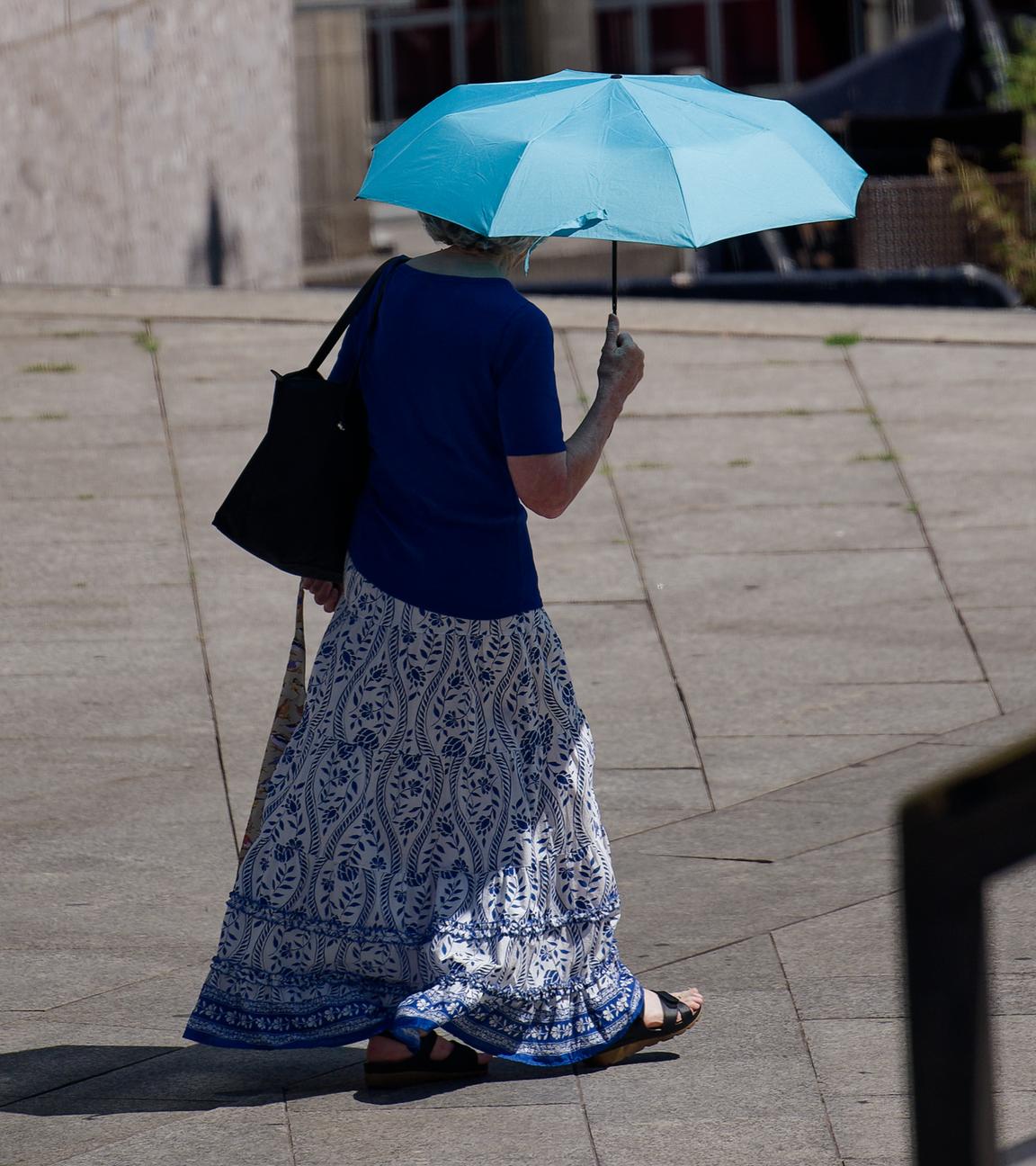 Köln: Eine Frau schützt sich mit einem Schirm vor der Sonne. 
