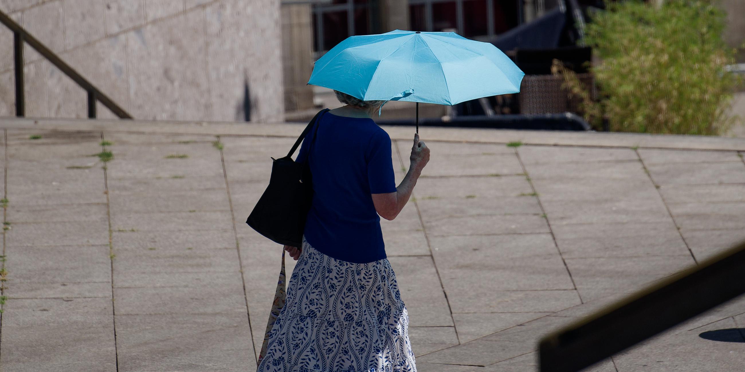 Köln: Eine Frau schützt sich mit einem Schirm vor der Sonne. 