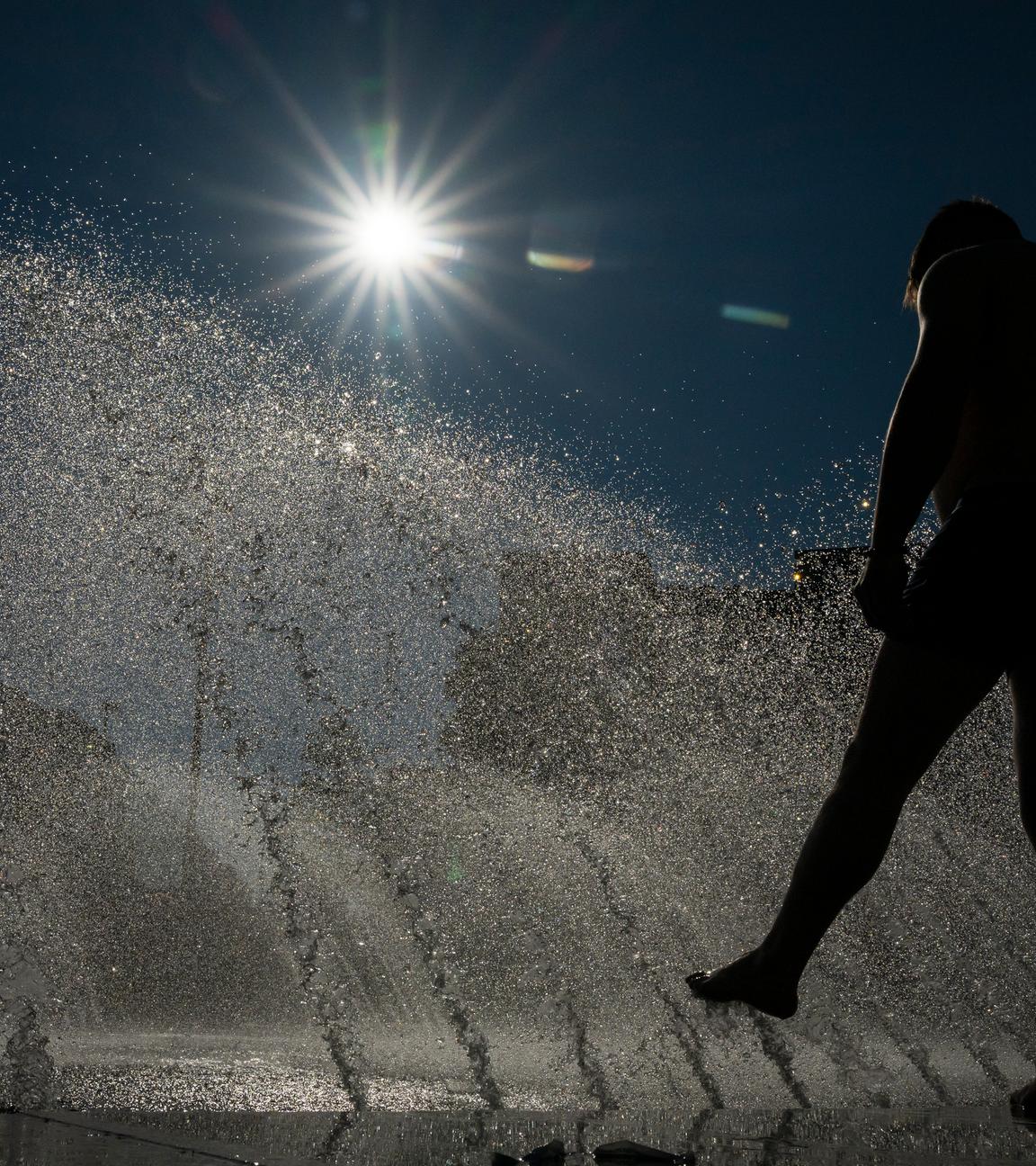 24.06.2025, Bayern, München: Ein Mann kühlt sich an einem Brunnen am Stachus in der Innenstadt im Wasser ab.