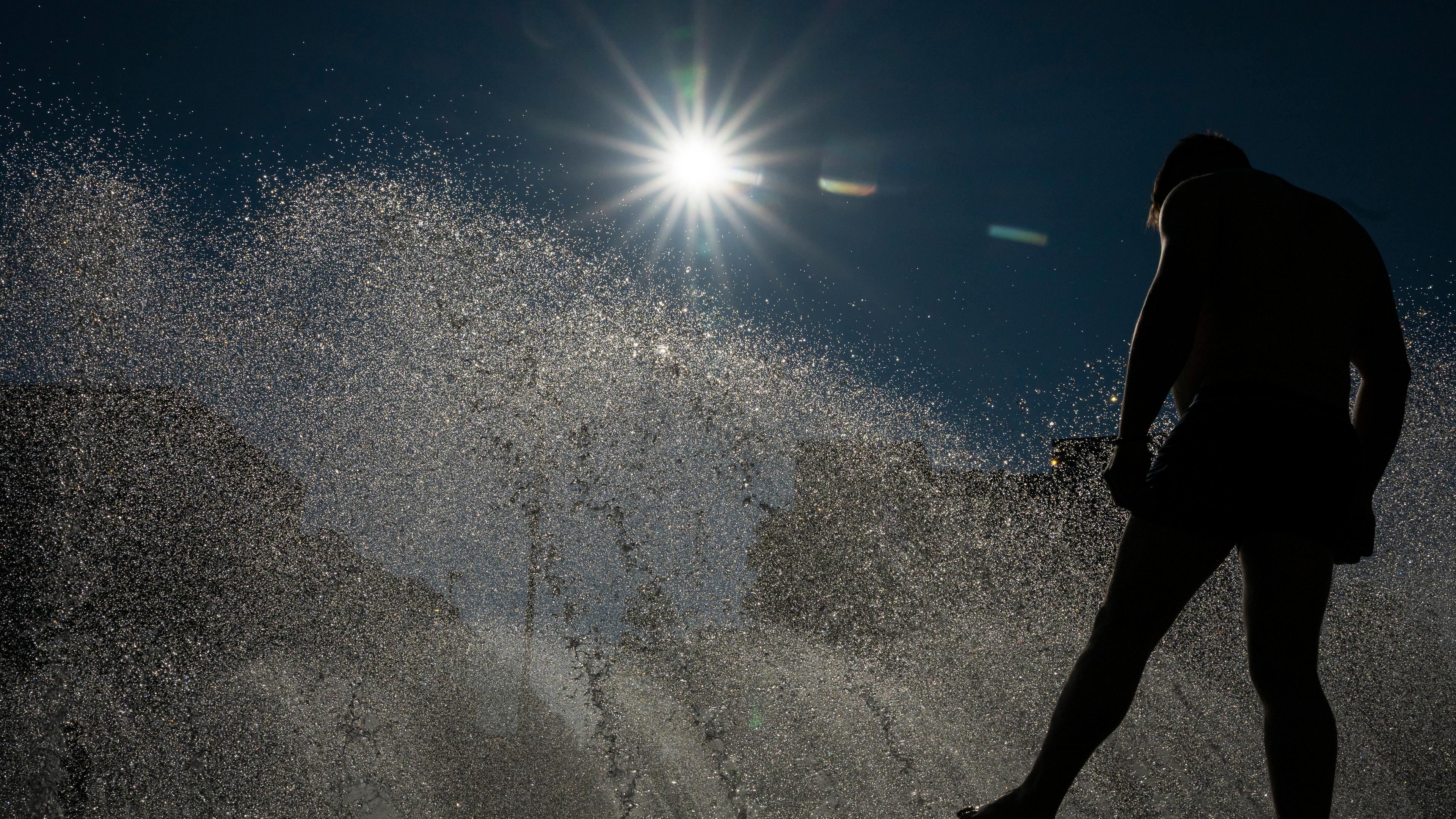 24.06.2025, Bayern, München: Ein Mann kühlt sich an einem Brunnen am Stachus in der Innenstadt im Wasser ab.