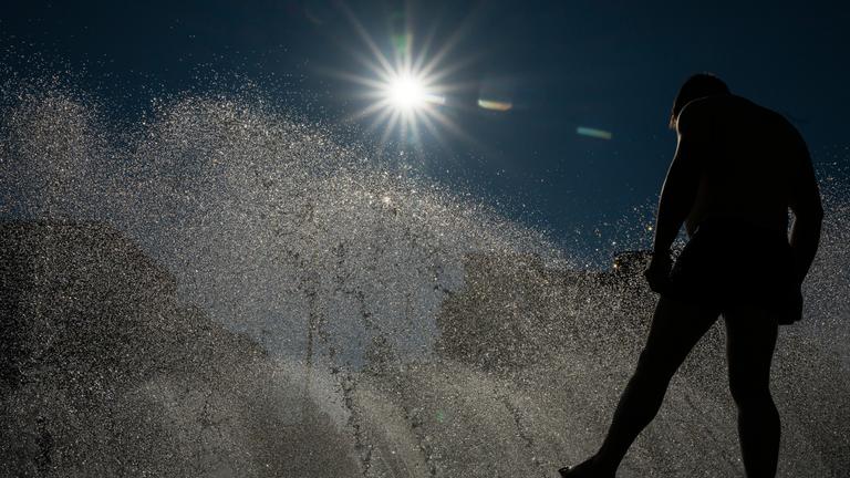 24.06.2025, Bayern, München: Ein Mann kühlt sich an einem Brunnen am Stachus in der Innenstadt im Wasser ab.
