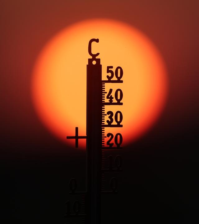 Hinter einem Thermometer geht am Morgen die Sonne auf
