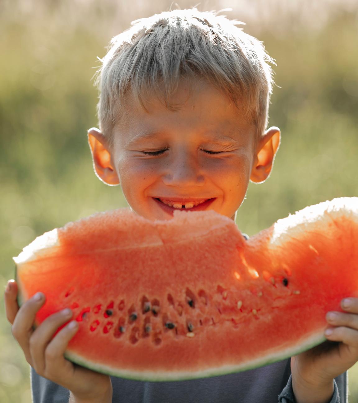 Ein junge isst ein Stück Wassermelone in der Sonne.