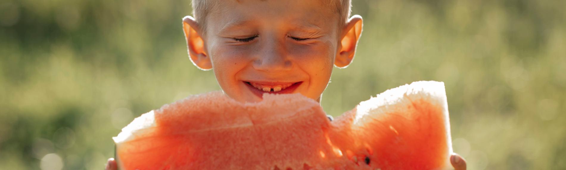 Ein junge isst ein Stück Wassermelone in der Sonne.