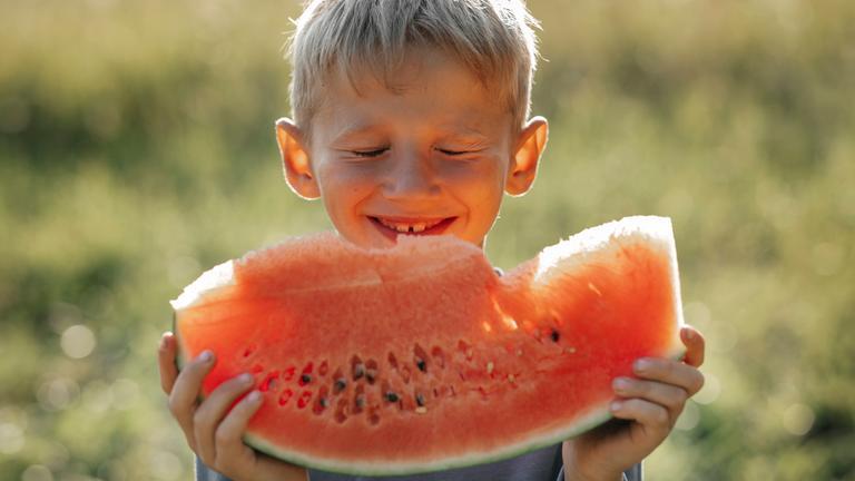 Ein junge isst ein Stück Wassermelone in der Sonne.