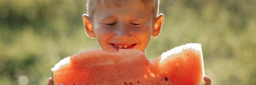 Ein junge isst ein Stück Wassermelone in der Sonne.