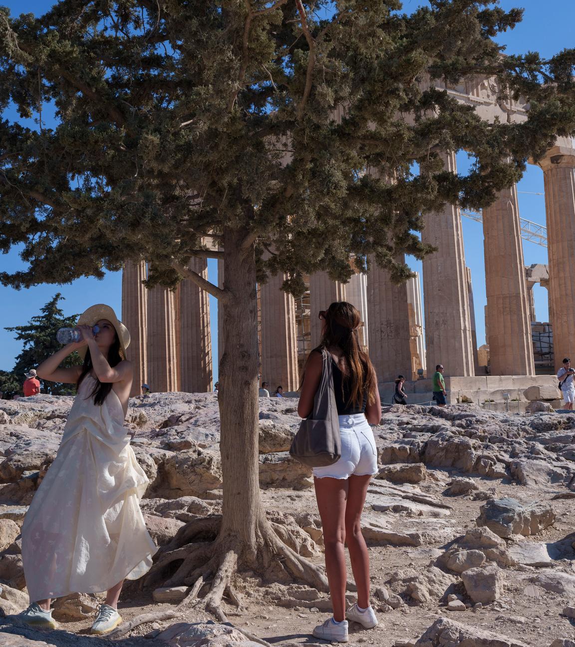 Eine Frau trinkt Wasser vor dem antiken Parthenon-Tempel an einem heißen, windigen Tag auf dem Akropolis-Hügel in Athen, 16.07.2024.