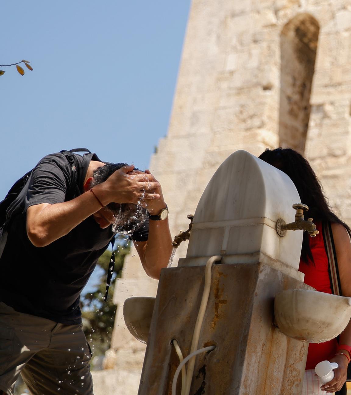 Griechenland, Athen: Ein Mann kühlt sich in der Nähe der Akropolis in Athen mit Wasser ab.