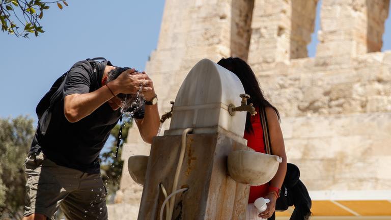 Griechenland, Athen: Ein Mann kühlt sich in der Nähe der Akropolis in Athen mit Wasser ab.