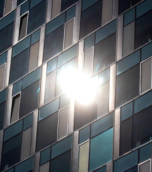 Symbolbild: Glasfassade eines Hochhauses reflektiert das Sonnenlicht