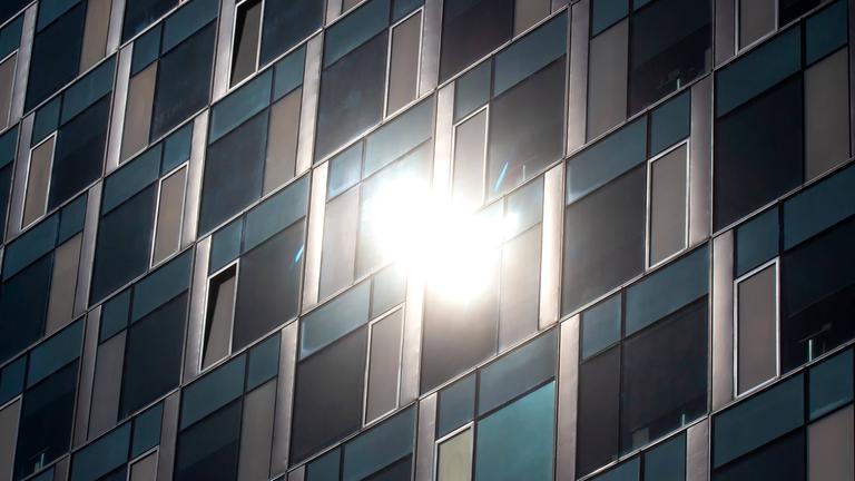 Symbolbild: Glasfassade eines Hochhauses reflektiert das Sonnenlicht