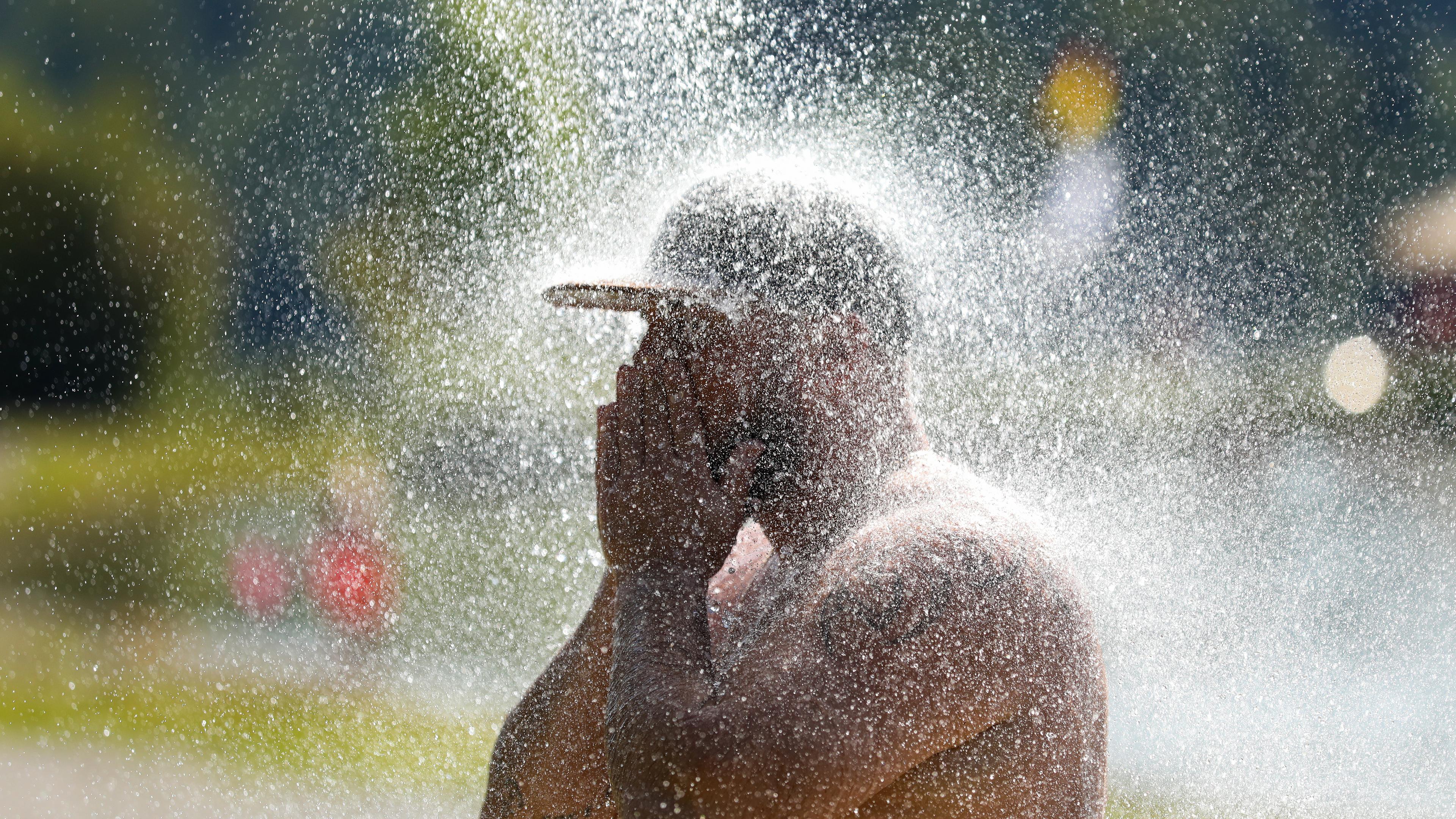 Ein Mann erfrischt sich an einem Badesee unter einer kalten Dusche.