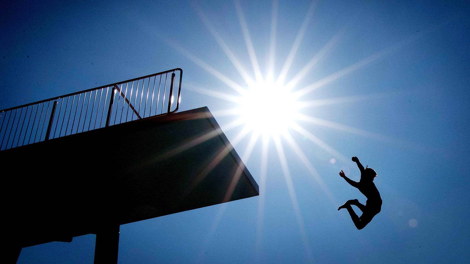 Abkühlung von der Hitze: Ein Mann springt vom Sprungturm in ein Schwimmbad-Becken.