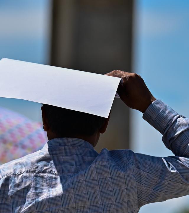 Ein Mann schützt sich vor dem Brandenburger Tor mit einem Blatt Papier gegen die Sonne.