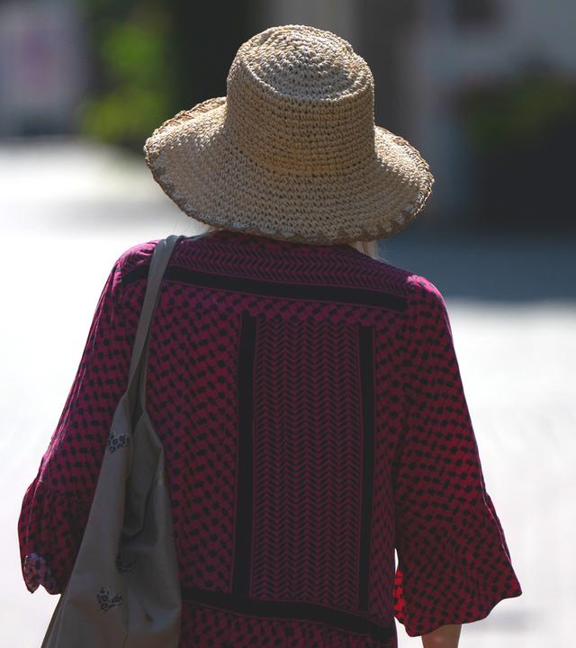 Eine Frau schützt sich mit einem Sonnenhut vor der Sonne.