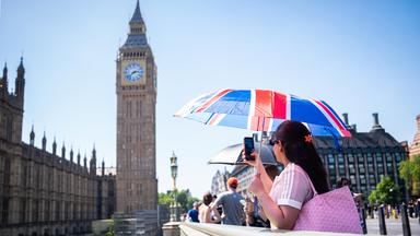 Eine Touristin macht ein Foto von Big Ben, während sie sich unter einem Union-Jack-Schirm auf der Westminster Bridge im Zentrum Londons vor der Hitze schützt, aufgenommen am 25.05.2026