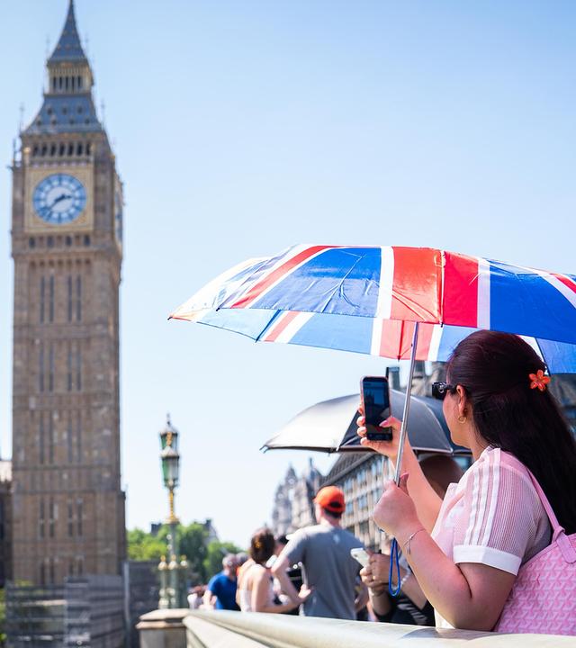 Eine Touristin macht ein Foto von Big Ben, während sie sich unter einem Union-Jack-Schirm auf der Westminster Bridge im Zentrum Londons vor der Hitze schützt, aufgenommen am 25.05.2026