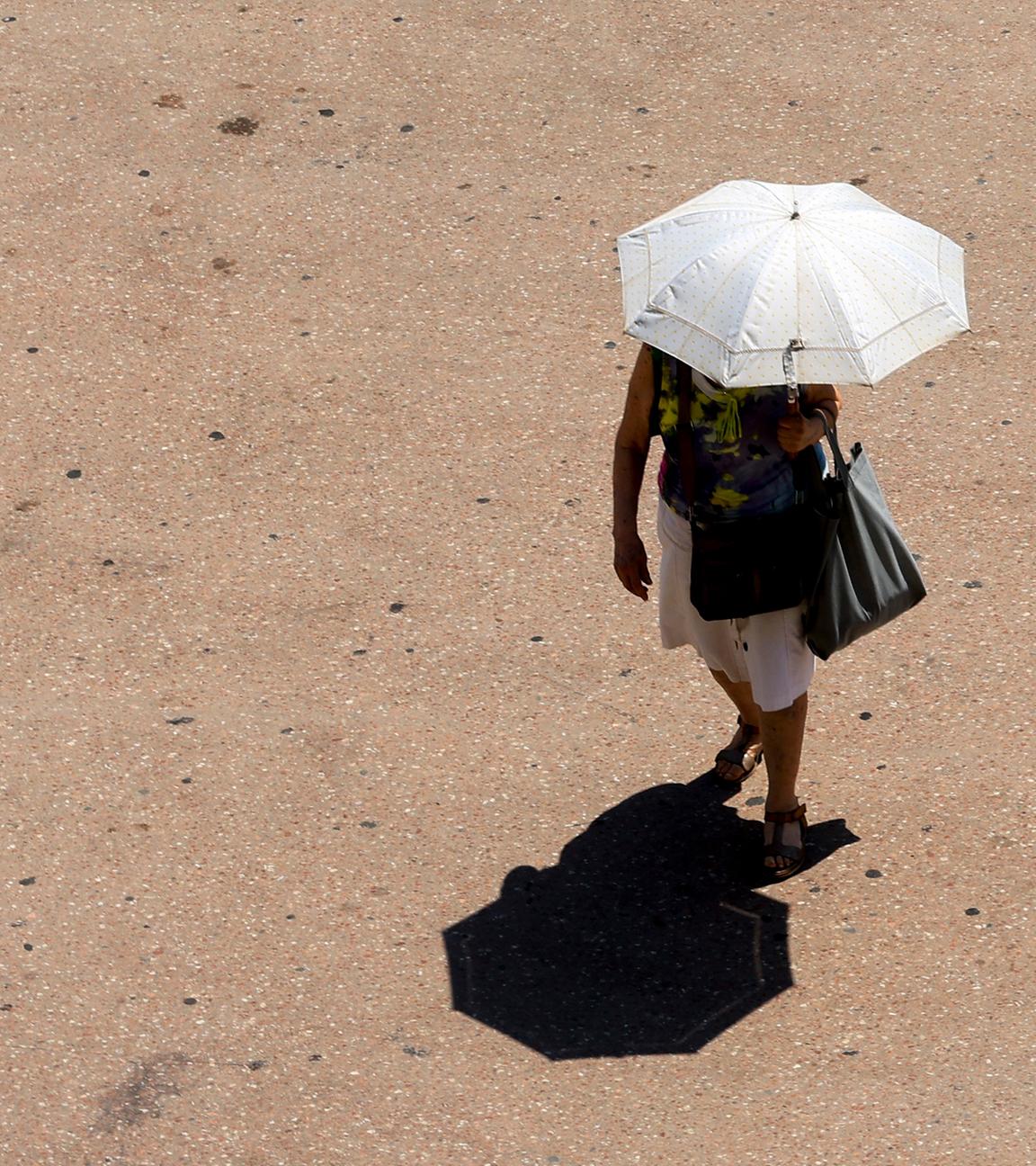Eine Frau geht mit einem Regenschirm zum Sonnenschutz auf einer Straße in Valencia