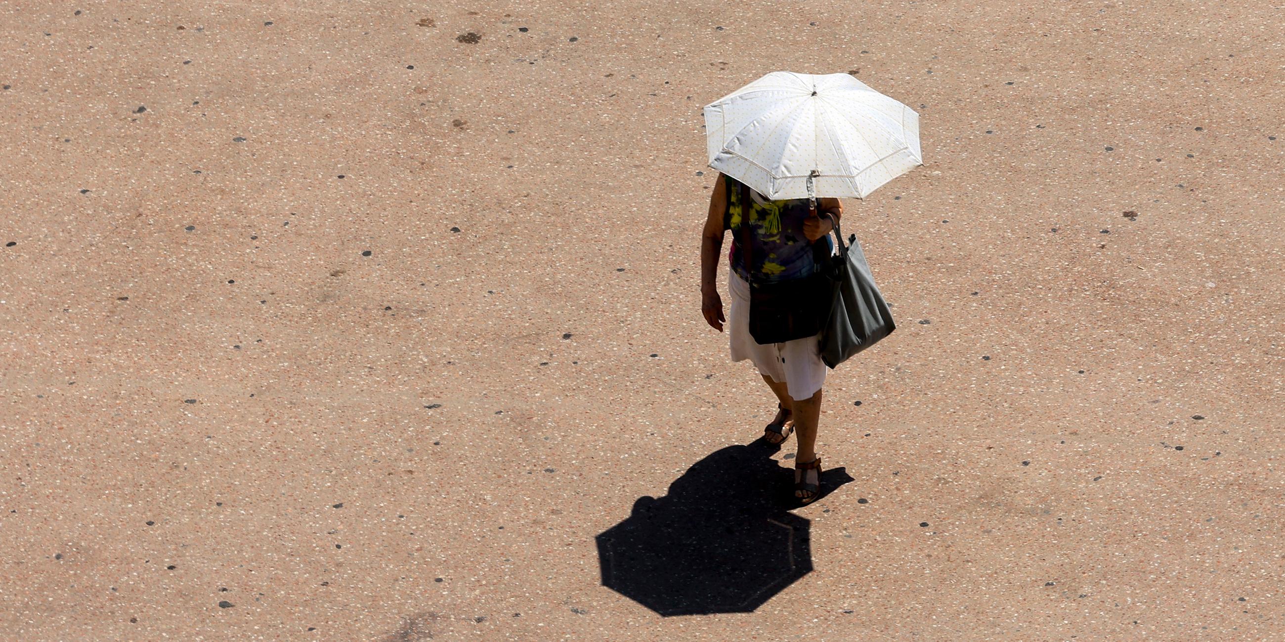 Eine Frau geht mit einem Regenschirm zum Sonnenschutz auf einer Straße in Valencia