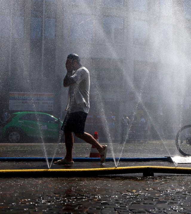 Passanten erfrischen sich an Wasserfontänen, die von der Stadt Köln im Rahmen der Hitzeaktion "Cooling Cologne" auf dem Rudolfplatz ausgelegt wurden.