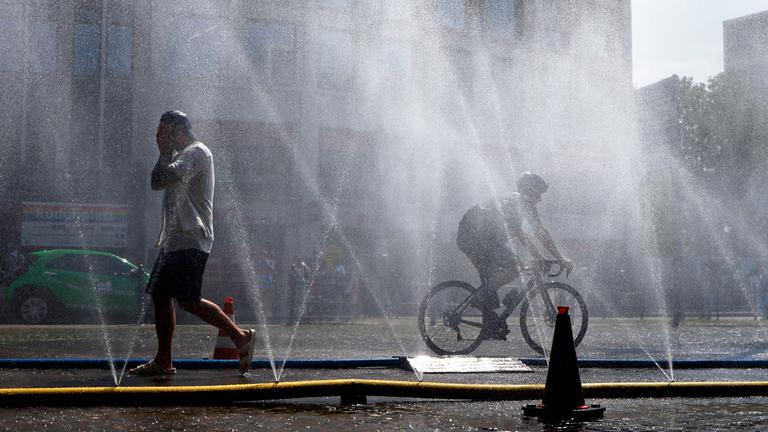 Passanten erfrischen sich an Wasserfontänen, die von der Stadt Köln im Rahmen der Hitzeaktion "Cooling Cologne" auf dem Rudolfplatz ausgelegt wurden.