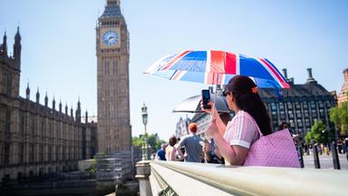 Großbritannien, London: Eine Touristin macht ein Foto von Big Ben (dem Elizabeth-Turm), während sie sich unter einem Union-Jack-Schirm auf der Westminster Bridge im Zentrum Londons vor der Hitze schützt.