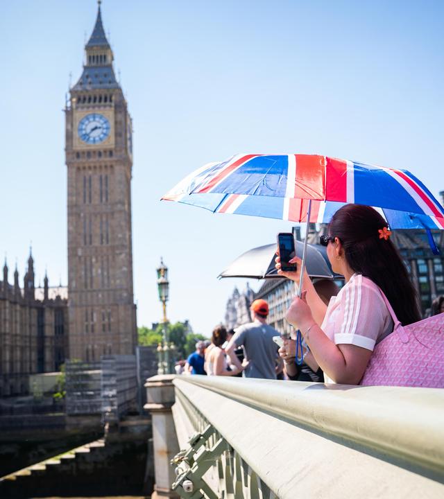 Großbritannien, London: Eine Touristin macht ein Foto von Big Ben (dem Elizabeth-Turm), während sie sich unter einem Union-Jack-Schirm auf der Westminster Bridge im Zentrum Londons vor der Hitze schützt.