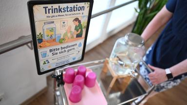Eine Frau schiebt in einem Pflegeheim einen Wagen mit Trinkbechern und Wasser. 