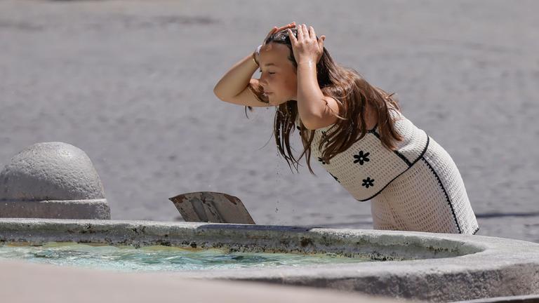 Hitze in Rom. Eine Frau kühlt sich am Brunnen ab