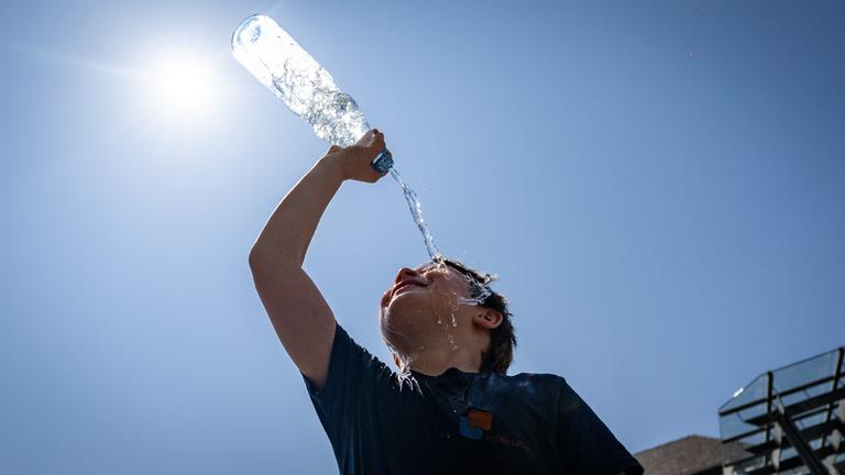 Ein Junge kühlt sich auf dem Bonner Marktplatz mit einer Flasche Wasser ab.