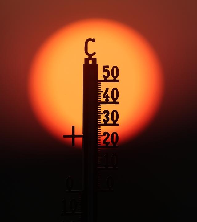 Hinter einem Thermometer geht am Morgen die Sonne auf.