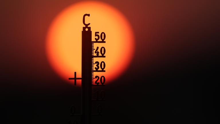 Hinter einem Thermometer geht am Morgen die Sonne auf.