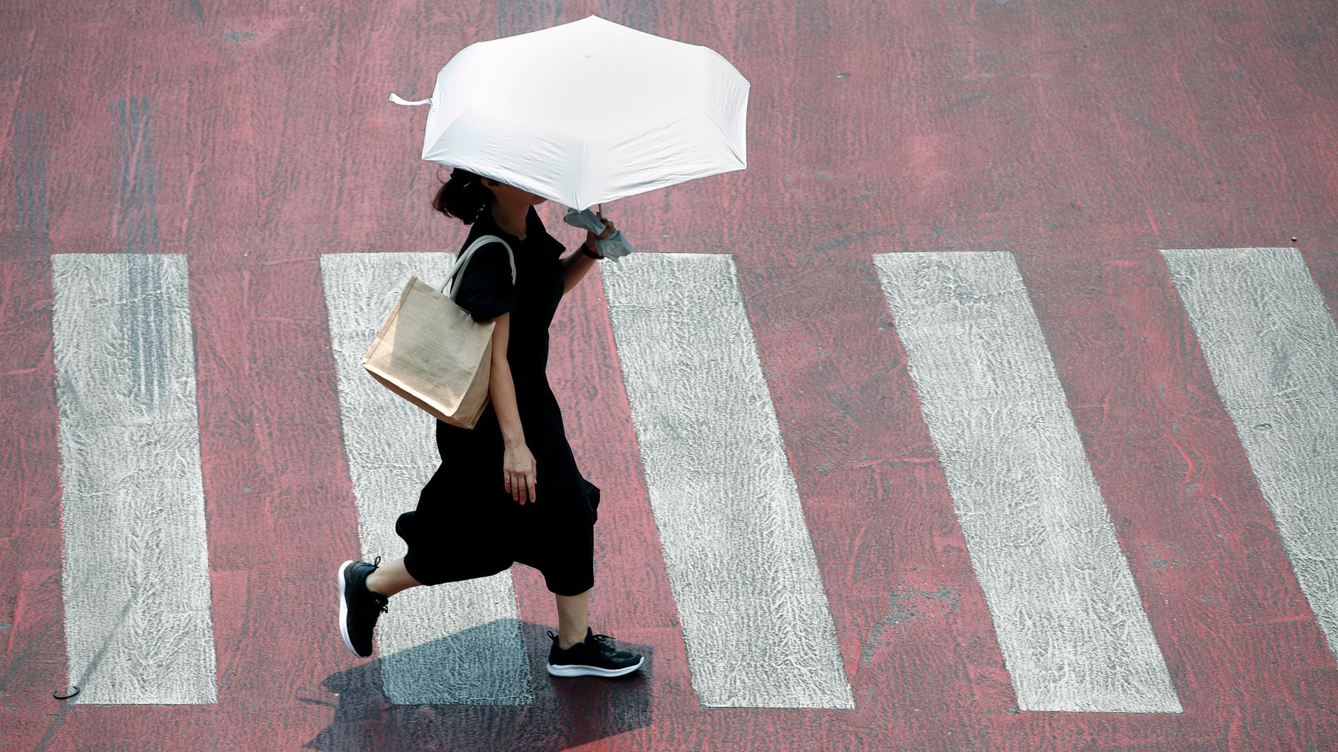 Ein Fußgänger benutzt einen Regenschirm, um sich vor der Sonne zu schützen, während er eine Straße bei heißem Wetter in Bangkok, Thailand, überquert, 01.05.2024.