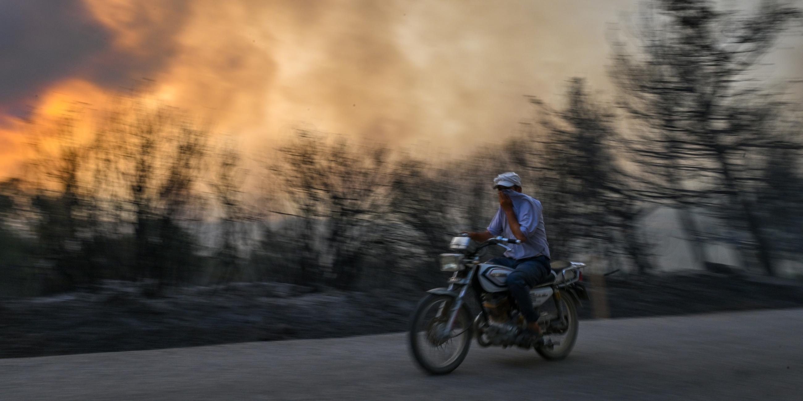 Ein Mann fährt mit seinem Motorrad, nachdem am 26.07.2023 in Izmir ein Feuer im Wald ausbrach und sich weiter ausbreitete. 