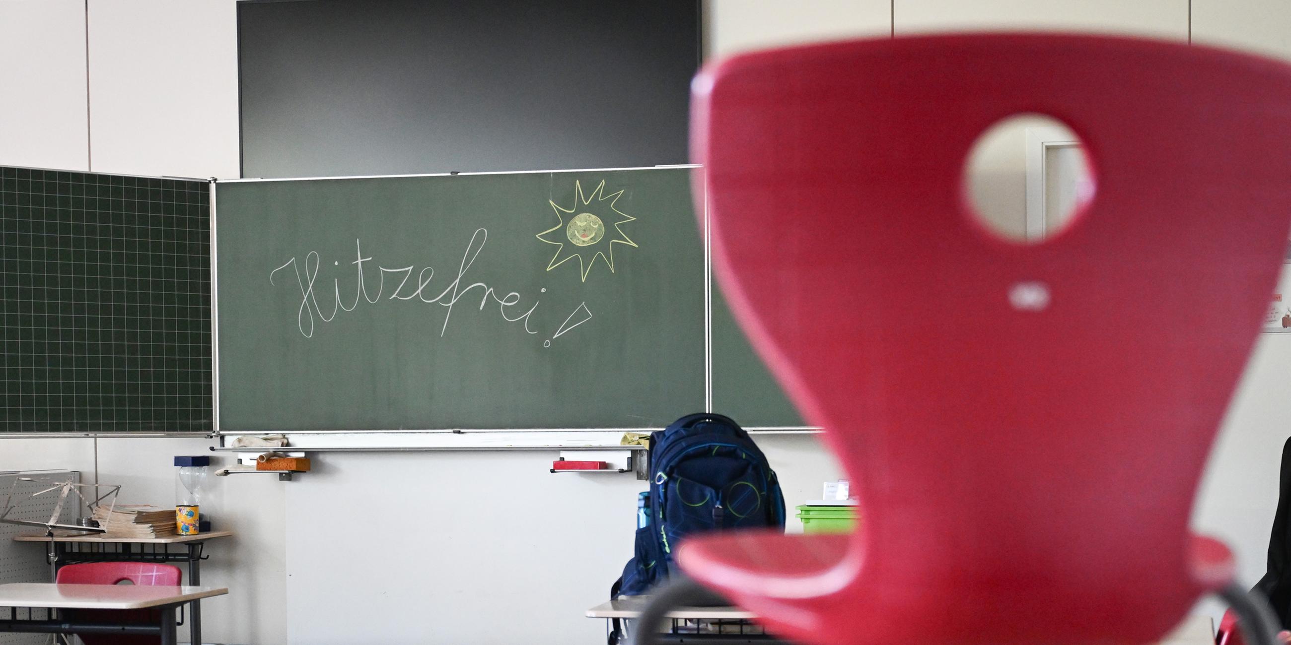 Das Wort "Hitzefrei" steht auf einer Tafel in einem leeren Klassenzimmer einer Grundschule. 