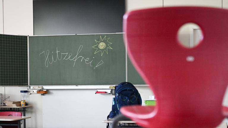 Das Wort "Hitzefrei" steht auf einer Tafel in einem leeren Klassenzimmer einer Grundschule. 
