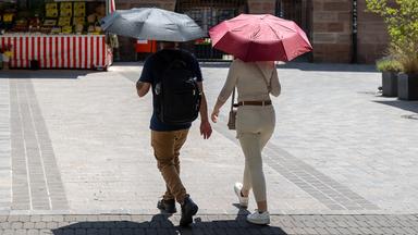 Archiv: Zwei Personen gehen mit geoeffneten Regenschirmen durch die sommerlich aufgeheizte Innenstadt von Nuernberg