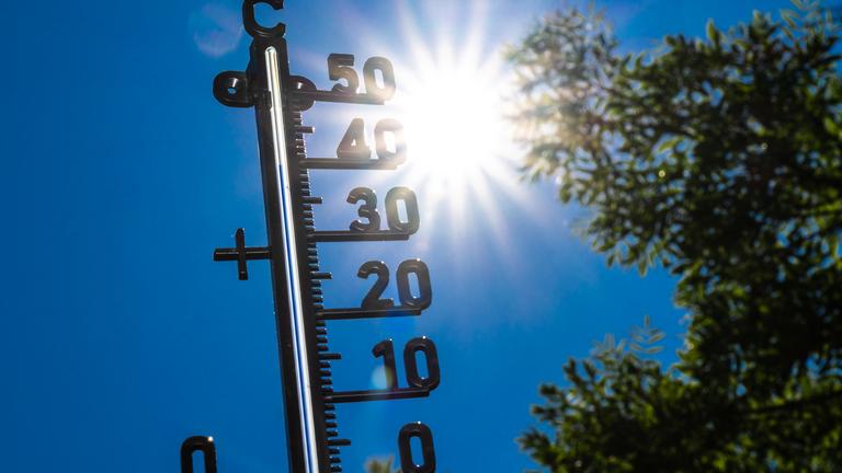 Ein Thermometer zeigt fast 40 Grad an. Im Hintergrund sind die Sonne und blauer Himmel zu sehen.