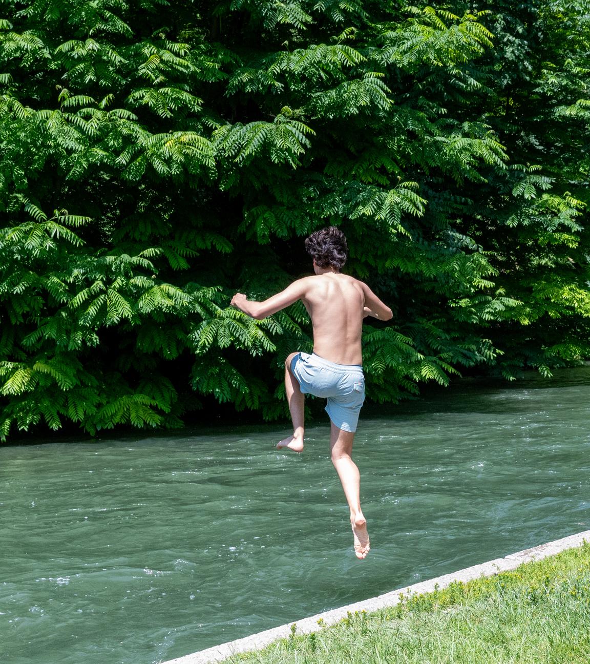 Zwei Kinder springen zur Abkühlung in ein Gewässer im Grünen