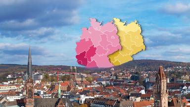 Über den Dächern einer Stadt sind zwei verschiedenfarbige Grafiken einer Deutschlandkarte abgebildet.