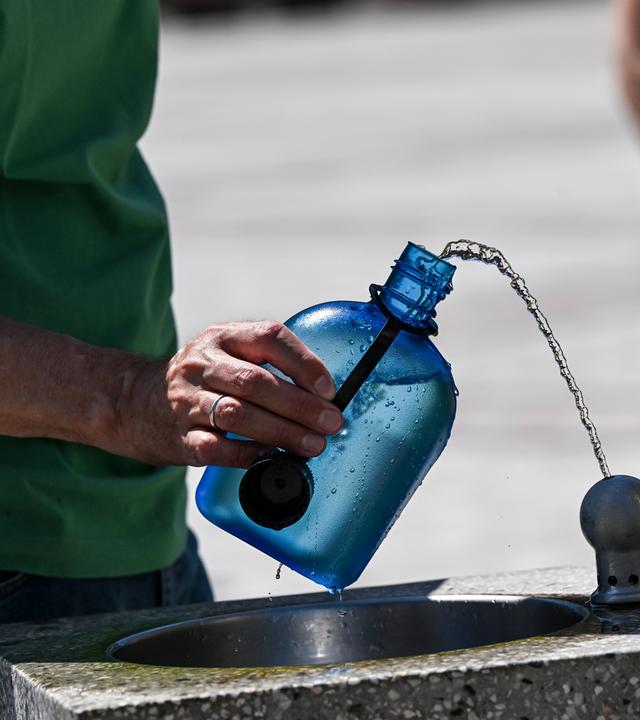 Ein Mann nutzt auf dem Gendarmenmarkt einen Wasserspender, um seine Trinkflasche aufzufüllen.