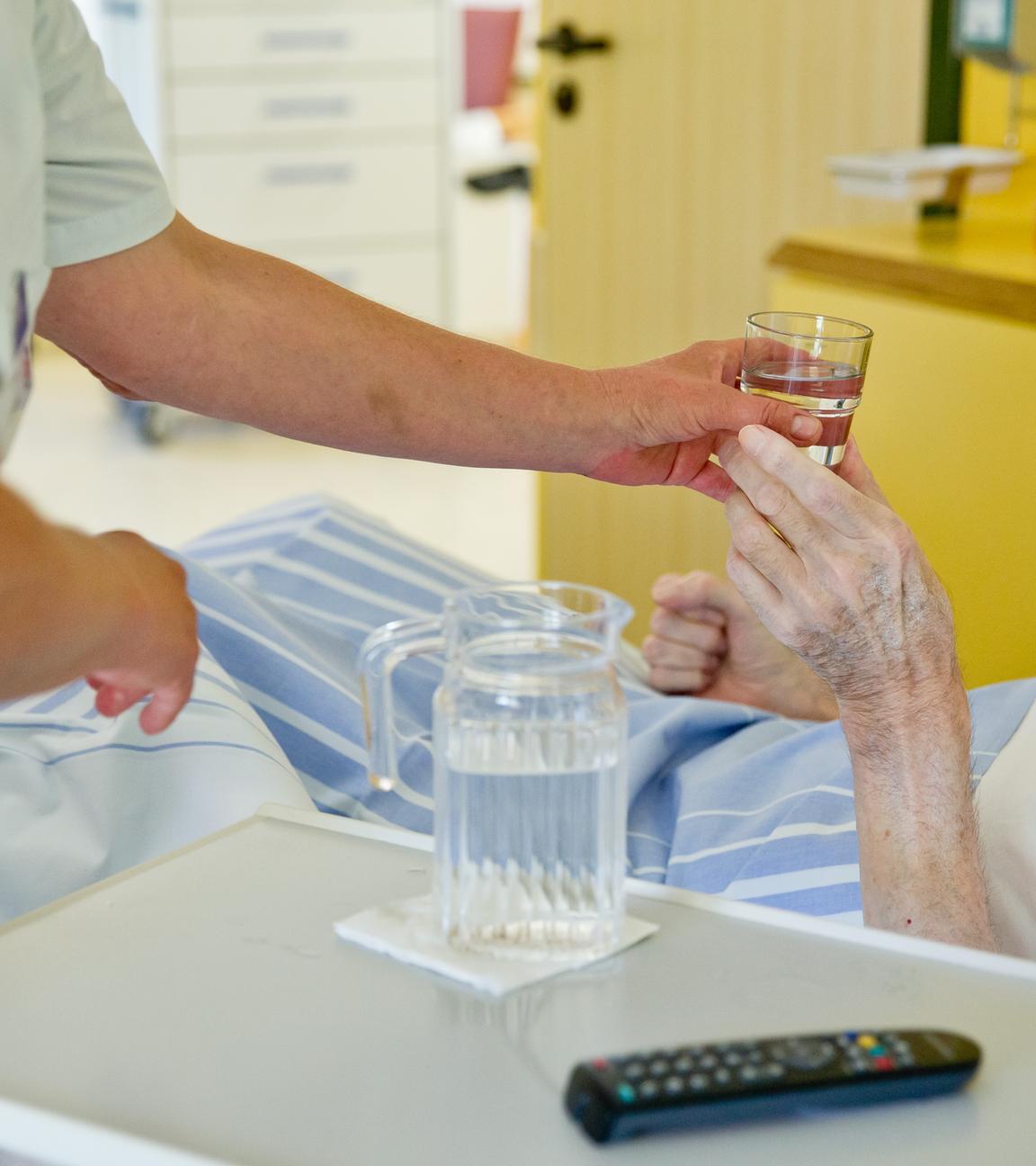 Eine Pflegerin reicht einer Patientin ein Glas Wasser