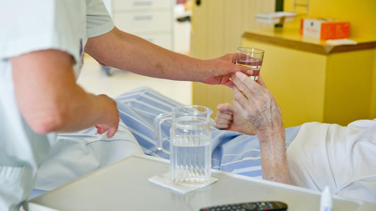 Eine Pflegerin reicht einer Patientin ein Glas Wasser